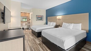A hotel room with two beds, a desk, a TV, and a bathroom visible in the background. - Baymont by Wyndham Orlando Downtown (Orlando)