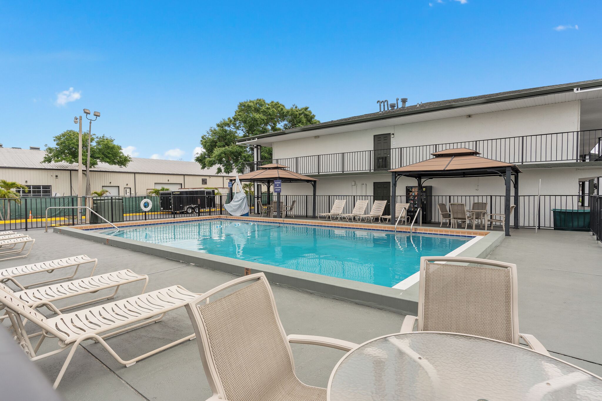 A swimming pool with lounge chairs and umbrellas, surrounded by a building with a balcony.