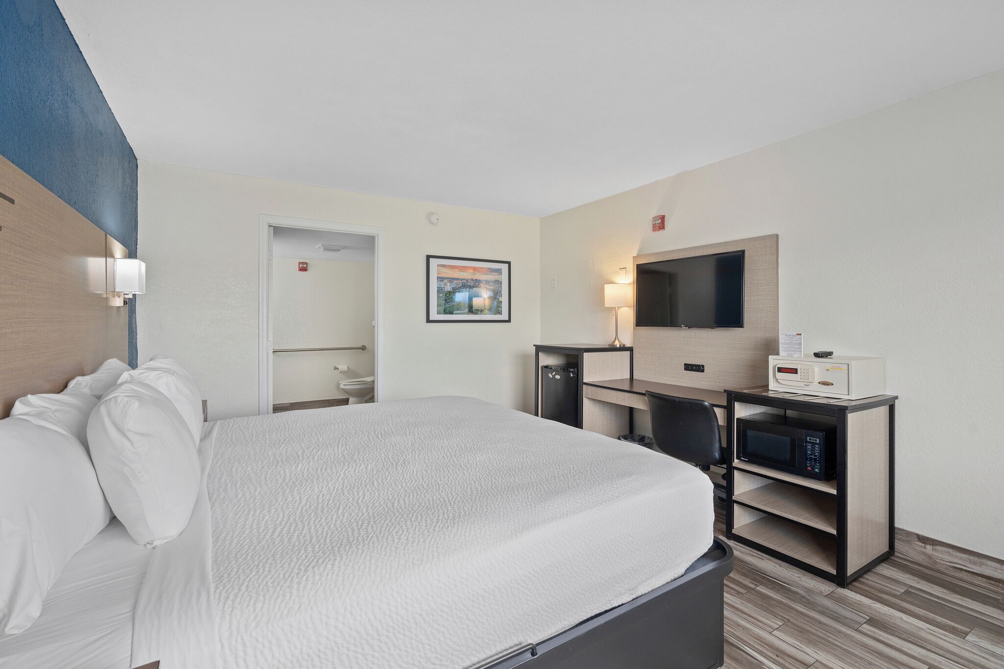 Habitación de hotel con cama, escritorio con microondas, televisión y un cuadro en la pared.