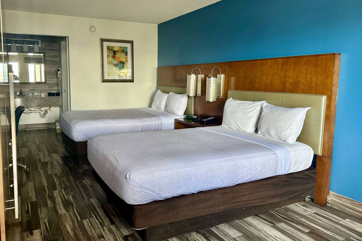 A hotel room with two beds, a wooden headboard, a painting on the wall, and a bathroom with a mirror and sink.