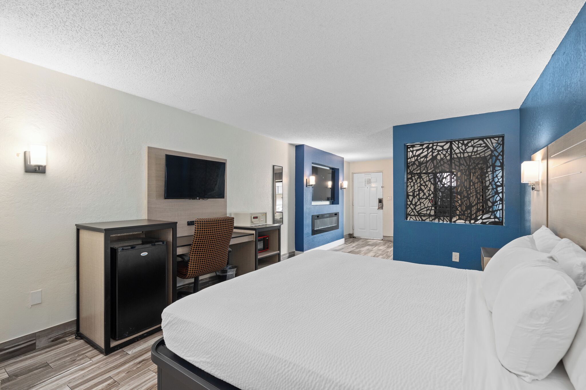 A hotel room with a bed, desk, and a small refrigerator.