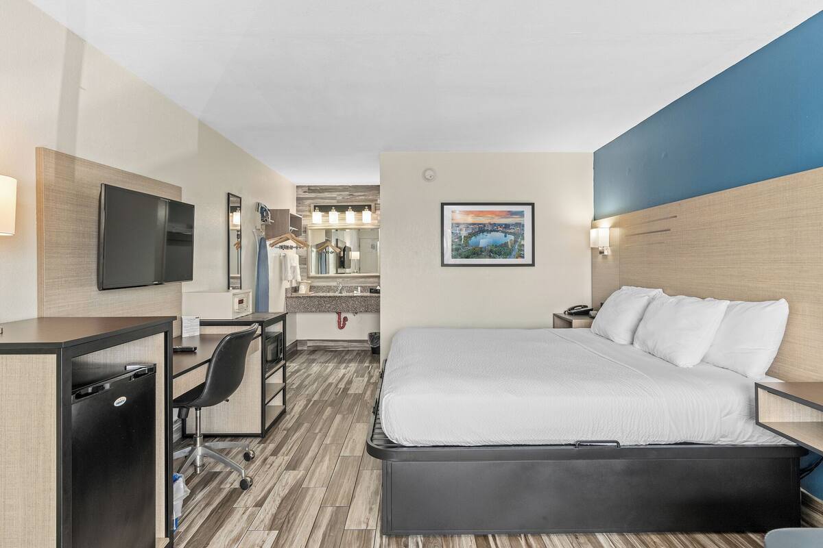 A hotel room with a bed, desk, chair, and a TV.