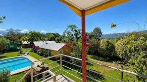A residential property with a swimming pool, a covered balcony, and a view of a green landscape with trees and a mountain in the distance.
