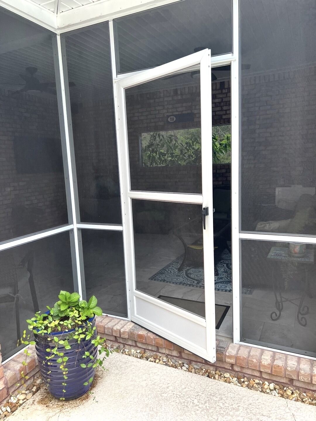 Een overdekt terras met een schuifpui, een bloempot en een bakstenen muur.