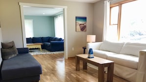 A living room with a blue sofa, a white sofa, a wooden coffee table, and a painting of a beach scene. - Perfect Family Getaway!  (Union Pier)