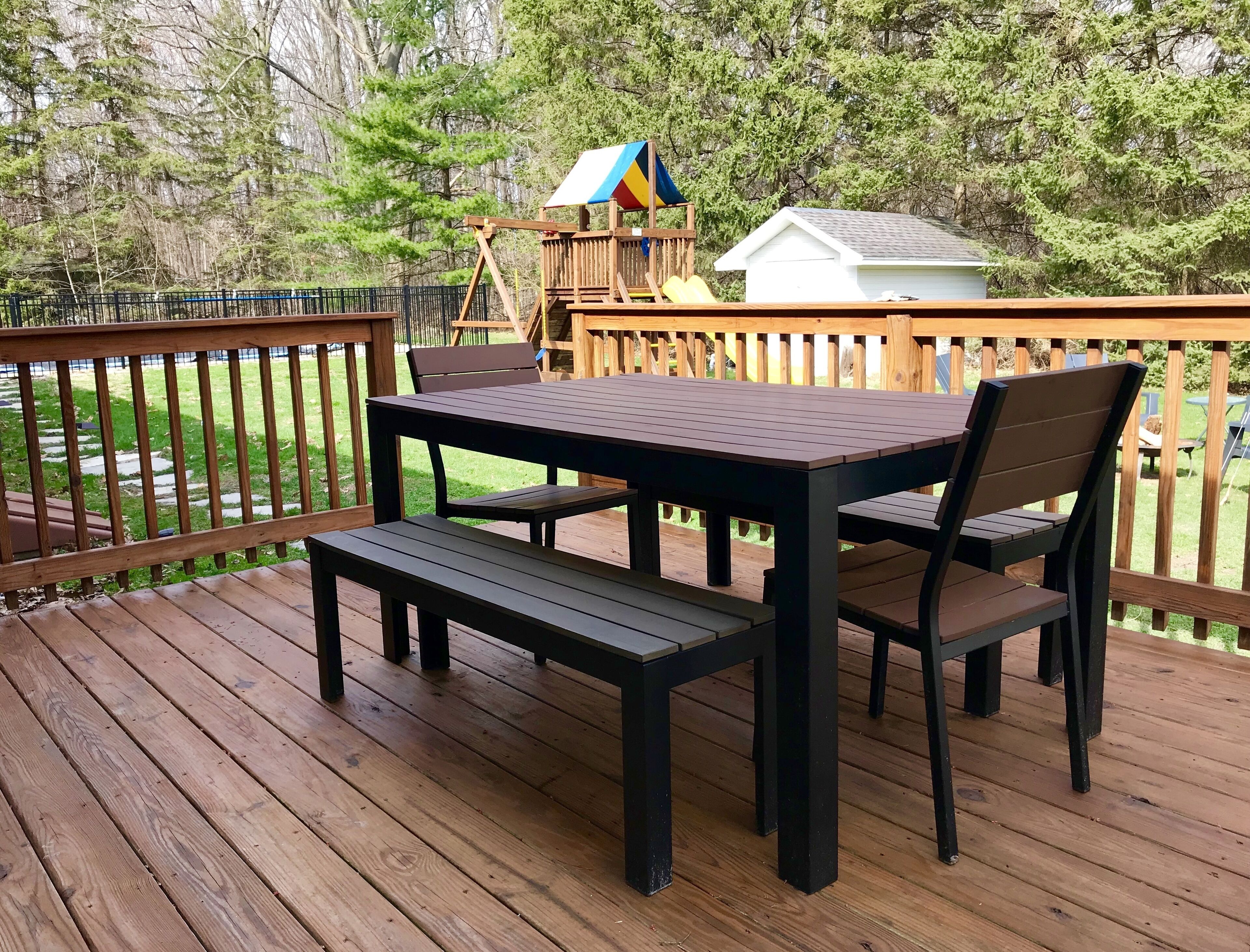A wooden deck with a table and chairs, a swing set, and a small shed.