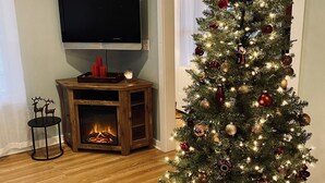 A living room with a Christmas tree, a fireplace, and a flat-screen TV mounted on the wall. - Perfect Family Getaway!  (Union Pier)