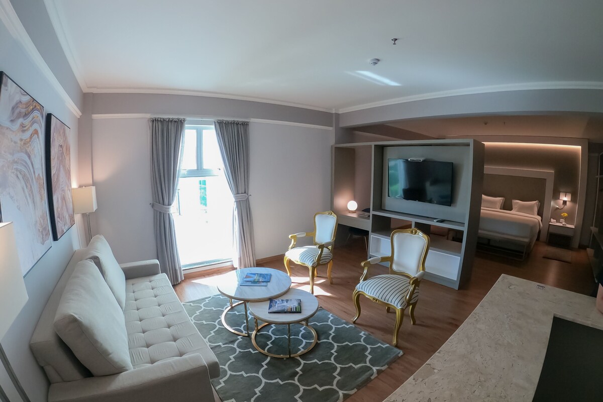 A modern living room with a sofa, two armchairs, a coffee table, a TV, and a bed.