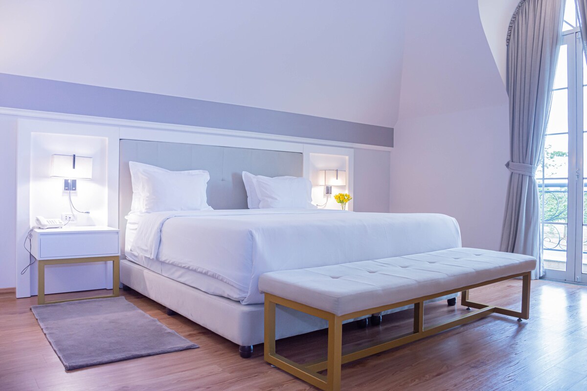 A modern bedroom with a large bed, bedside tables, a bench, and a view of the outdoors.