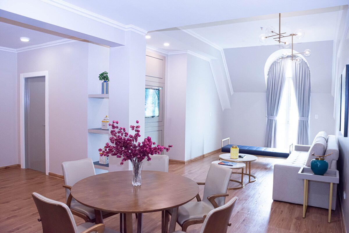 A modern living room with a round wooden table, white chairs, a sofa, and a blue vase.