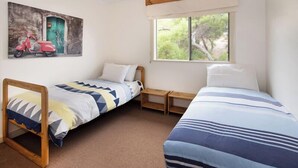 Quarto com duas camas de solteiro, janela com vista para vegetação, quadro de uma scooter na parede e cabeceira de madeira.