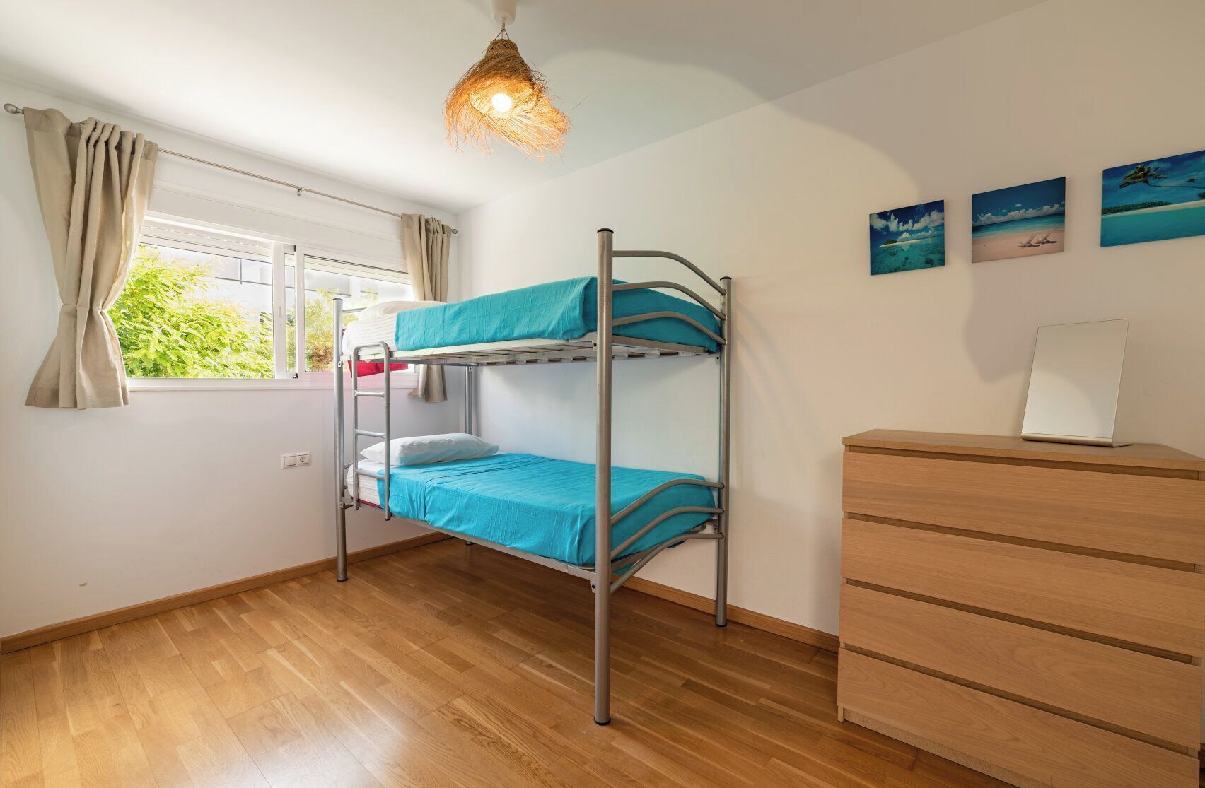 A room with a bunk bed, wooden dresser, and a window with curtains.