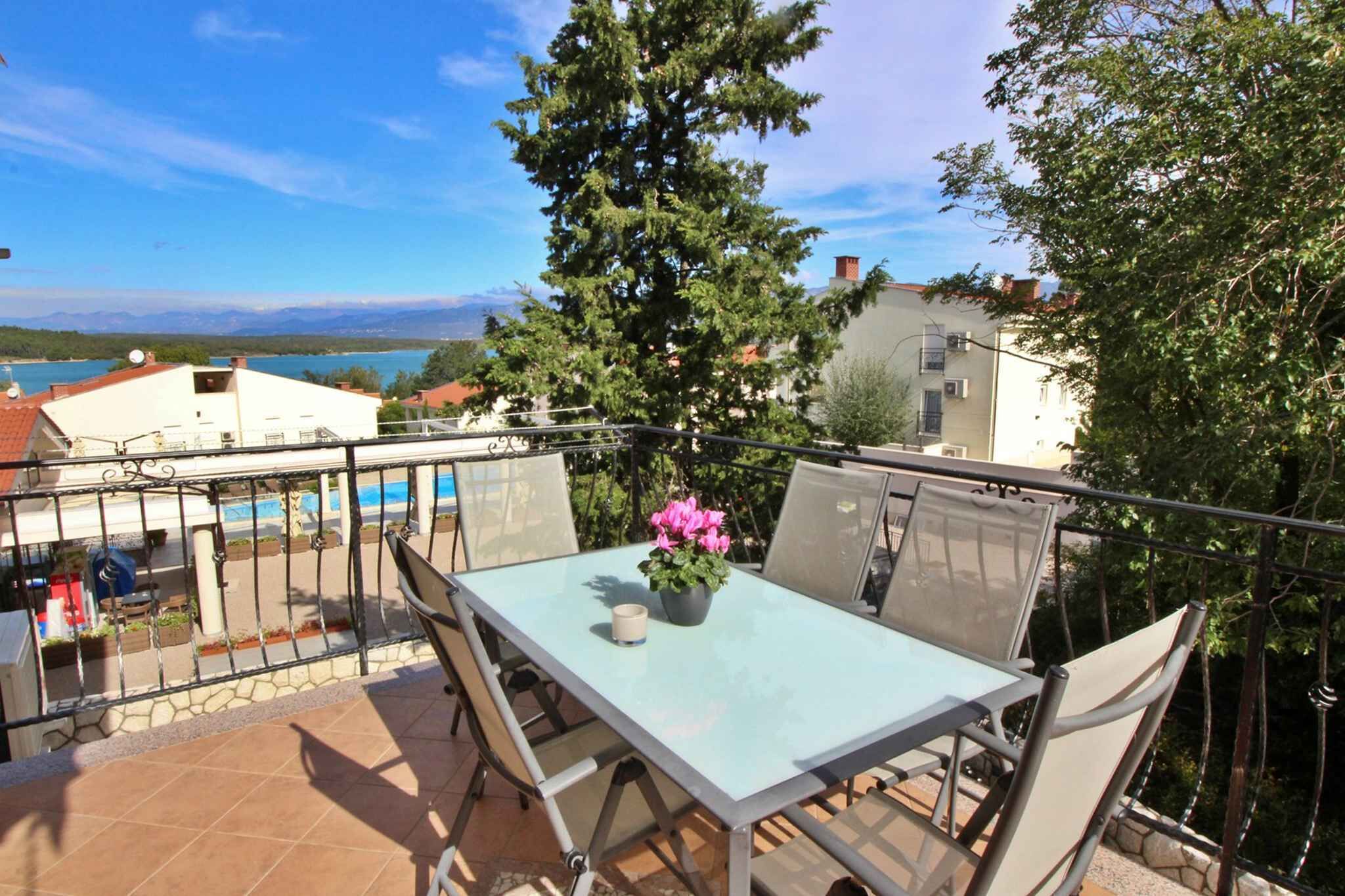 A balcony with a table and chairs, a potted plant, and a view of a lake and mountains.