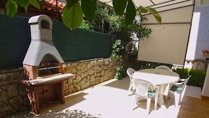 Um pátio externo com parede de pedra, forno a pizza e mesa com cadeiras.