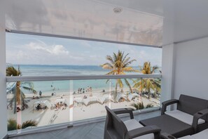 A balcony with a view of a beach, wicker furniture, and a glass railing. - Molino De Viento (San Andrés)