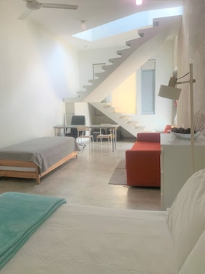 A modern room with a bed, a desk, a red sofa, and a staircase leading to an upper level.