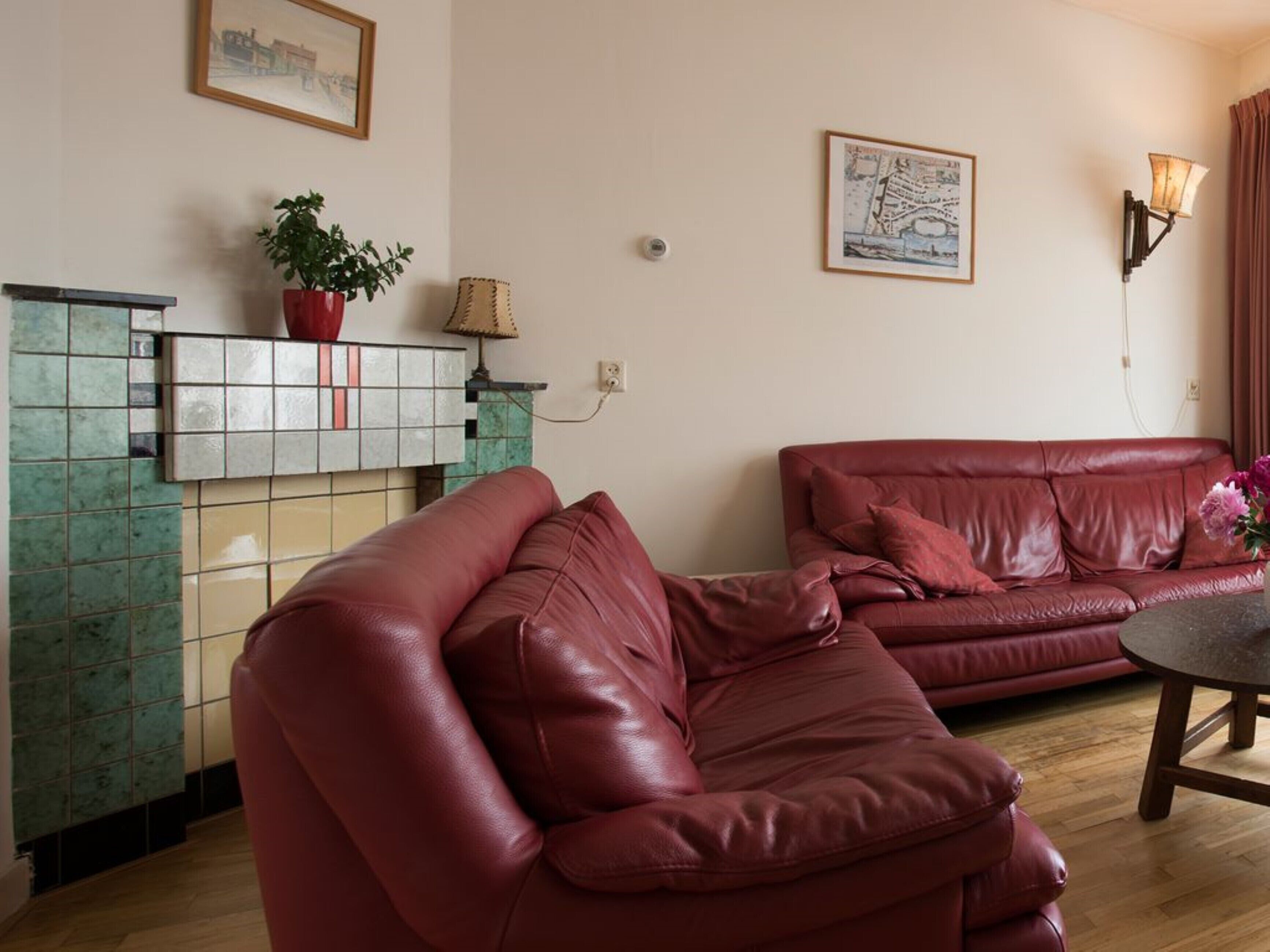 Ein Wohnzimmer mit einem roten Ledersofa, einem kleinen Tisch mit einer Vase und einem gekachelten Kamin.