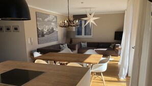 Une cuisine moderne avec un îlot central en bois, des chaises blanches, une table à manger et un luminaire en forme d’étoile.