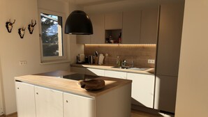 Une cuisine moderne dotée d’un îlot central, de meubles blancs, d’un luminaire suspendu noir et d’une fenêtre donnant sur la verdure.