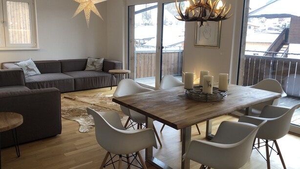 Un salon moderne avec une table à manger en bois, des chaises blanches, un canapé gris et un luminaire en forme d’étoile.