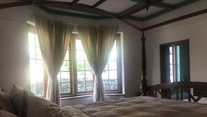A bedroom with a large bed, a wooden headboard, and a window with curtains. - Full board on an organic tea estate high in the hills - whole cottage with staff (Hildummulla)