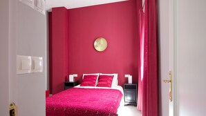 A bedroom with a red wall, a round gold clock, and a bed with white and pink bedding. - Triana Terrace. 1-bedroom, roof-top terrace (Sevilla)