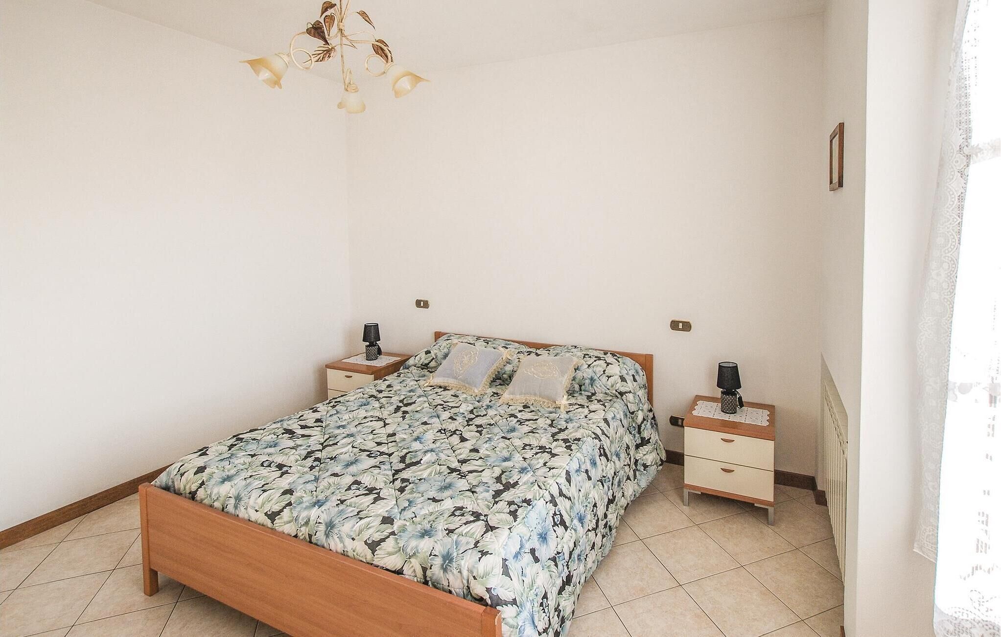 A bedroom with a wooden bed, floral bedding, two bedside tables with lamps, and a chandelier.