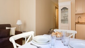 Un comedor con una mesa preparada para dos personas, un sofá, una lámpara y una cocina al fondo.