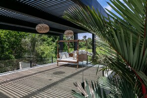 An outdoor seating area with a wooden swing bed and a woven hanging light fixture.