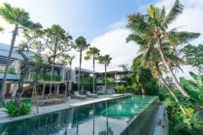 A pool area with lounge chairs, palm trees, and a modern building with balconies.