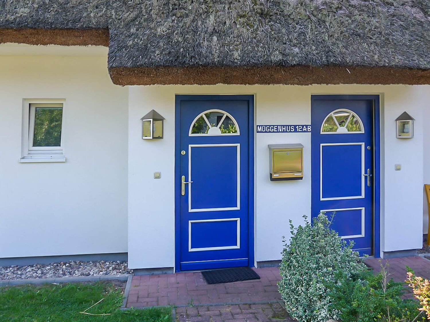 Un bâtiment avec deux portes bleues, chacune surmontée d’une petite fenêtre. Une boîte aux lettres est fixée au mur, entre les deux portes.