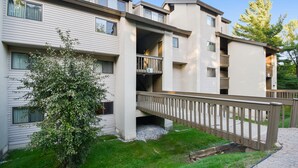 A multi-story residential building with balconies, a covered walkway, and a small tree in the foreground. - Pinnacle A5 Condo | Pool, Hot Tub | Golf Nearby (Killington)