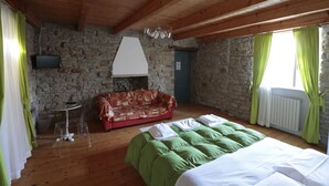Une pièce avec un mur en pierre, un plafond en bois, un lit avec une literie verte, un canapé rouge, une petite table avec une chaise et un téléviseur fixé au mur.