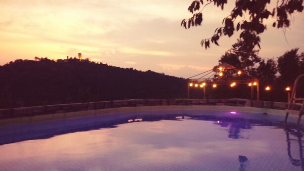 Une piscine au crépuscule, illuminée par des lumières disposées tout autour, avec une colline en arrière-plan.
