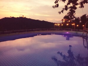 Une piscine au crépuscule, illuminée par des lumières disposées tout autour, avec une colline en arrière-plan.