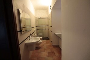 Un baño pequeño con lavamanos, dos inodoros, ducha y espejo.