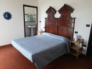 Un dormitorio con cabecera de madera, una cama con colcha azul, una mesita de noche con lámpara y una silla de madera.