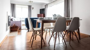 Un comedor moderno con una mesa de madera, sillas blancas y un televisor al fondo.