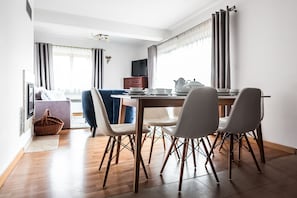 A modern dining area with a wooden table, white chairs, and a television in the background.