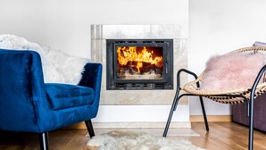 Una habitación con chimenea, una silla azul, una silla de mimbre y una alfombra de piel.