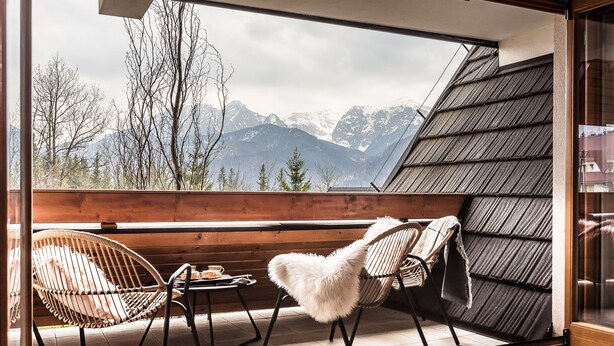 Un balcón con vista a montañas, una mesa de madera y dos sillas.