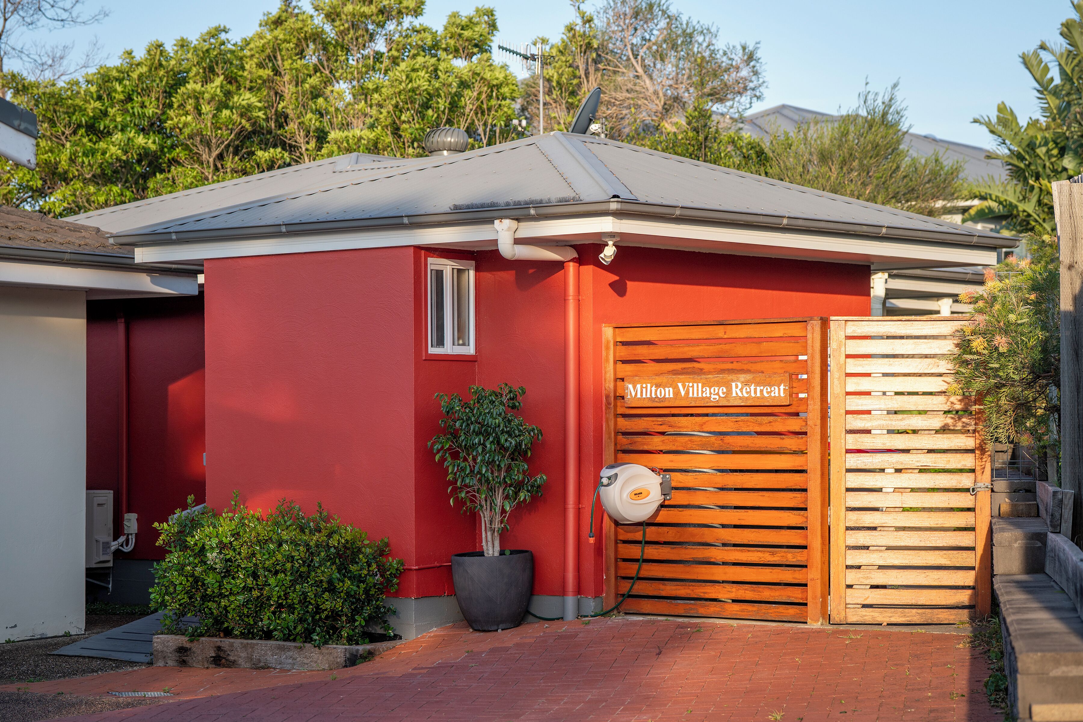 A red building with a wooden gate labeled "Milton Village Retreat."