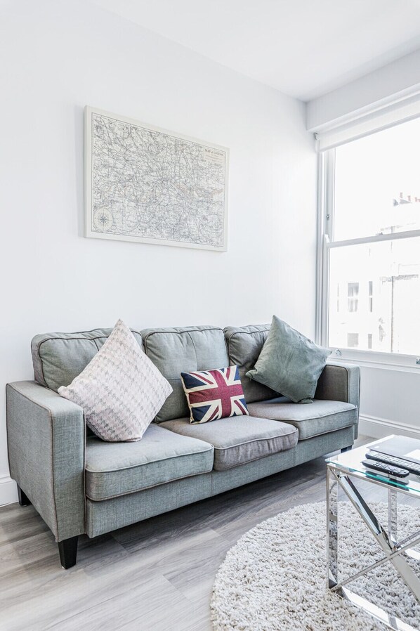 A modern living room with a grey sofa, patterned cushions, a map artwork, and a glass coffee table.