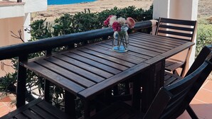 Une table en bois, entourée de chaises, et un vase de fleurs, le tout placé devant un mur blanc avec vue sur la mer.