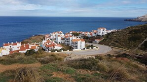 Un village côtier aux bâtiments blancs et aux toits rouges, avec une route sinueuse et une vue sur la mer.