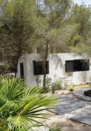 Un bâtiment blanc avec des volets noirs, entouré d’arbres et de plantes.