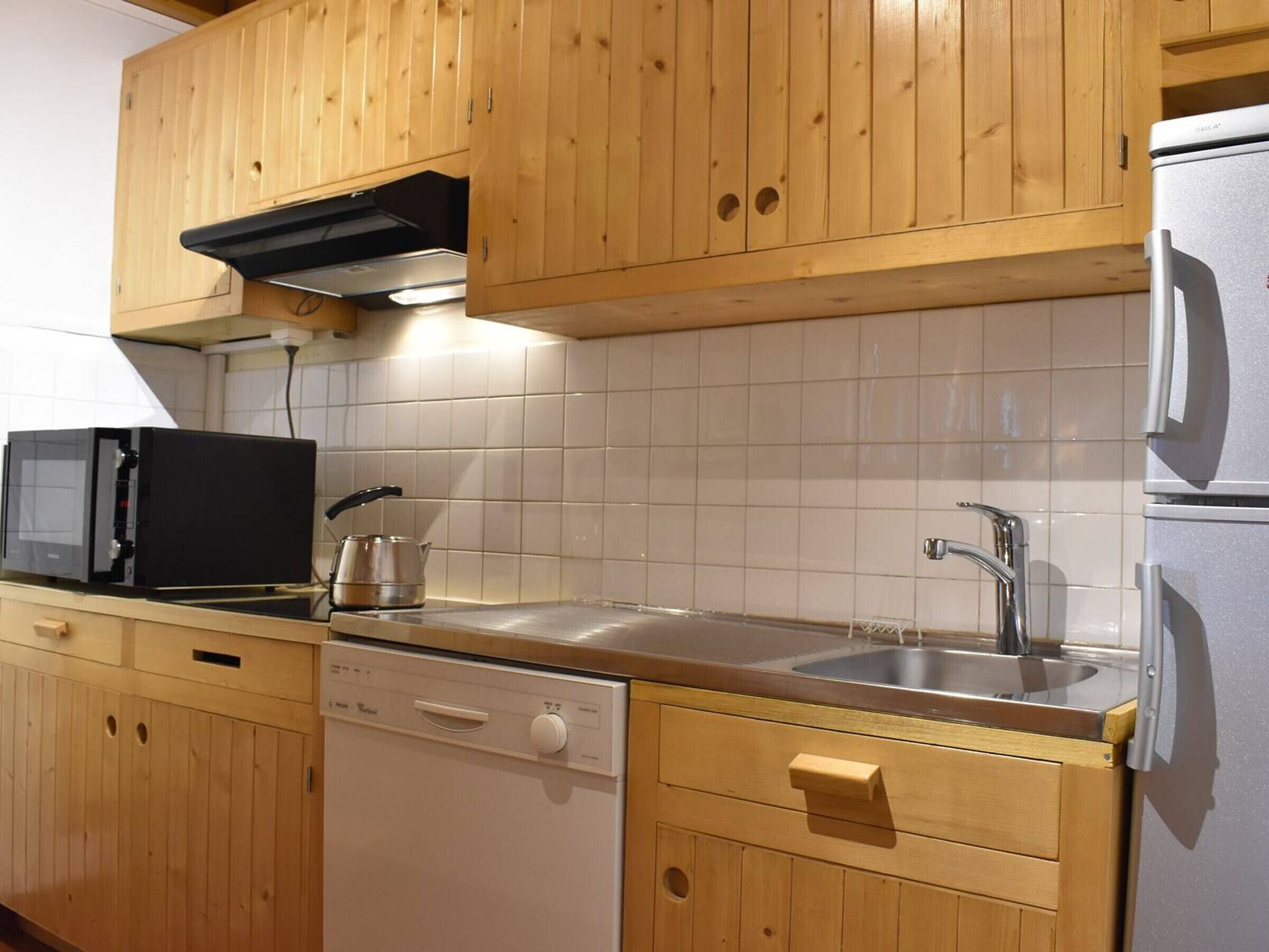 A kitchen with wooden cabinets, a microwave, a dishwasher, a sink, and a refrigerator.