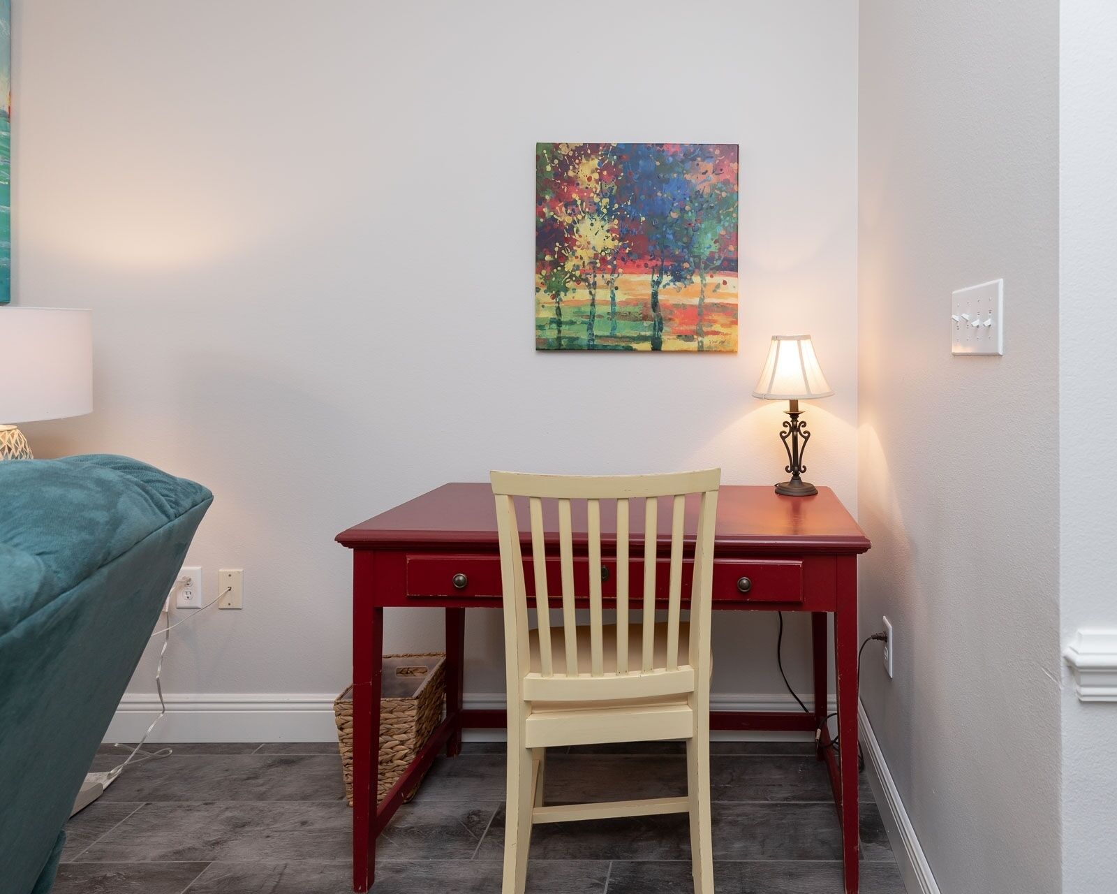A small room with a desk, chair, and a painting on the wall.