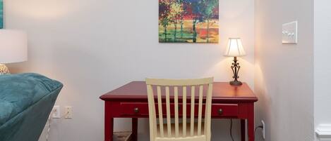 A small room with a desk, chair, and a painting on the wall.