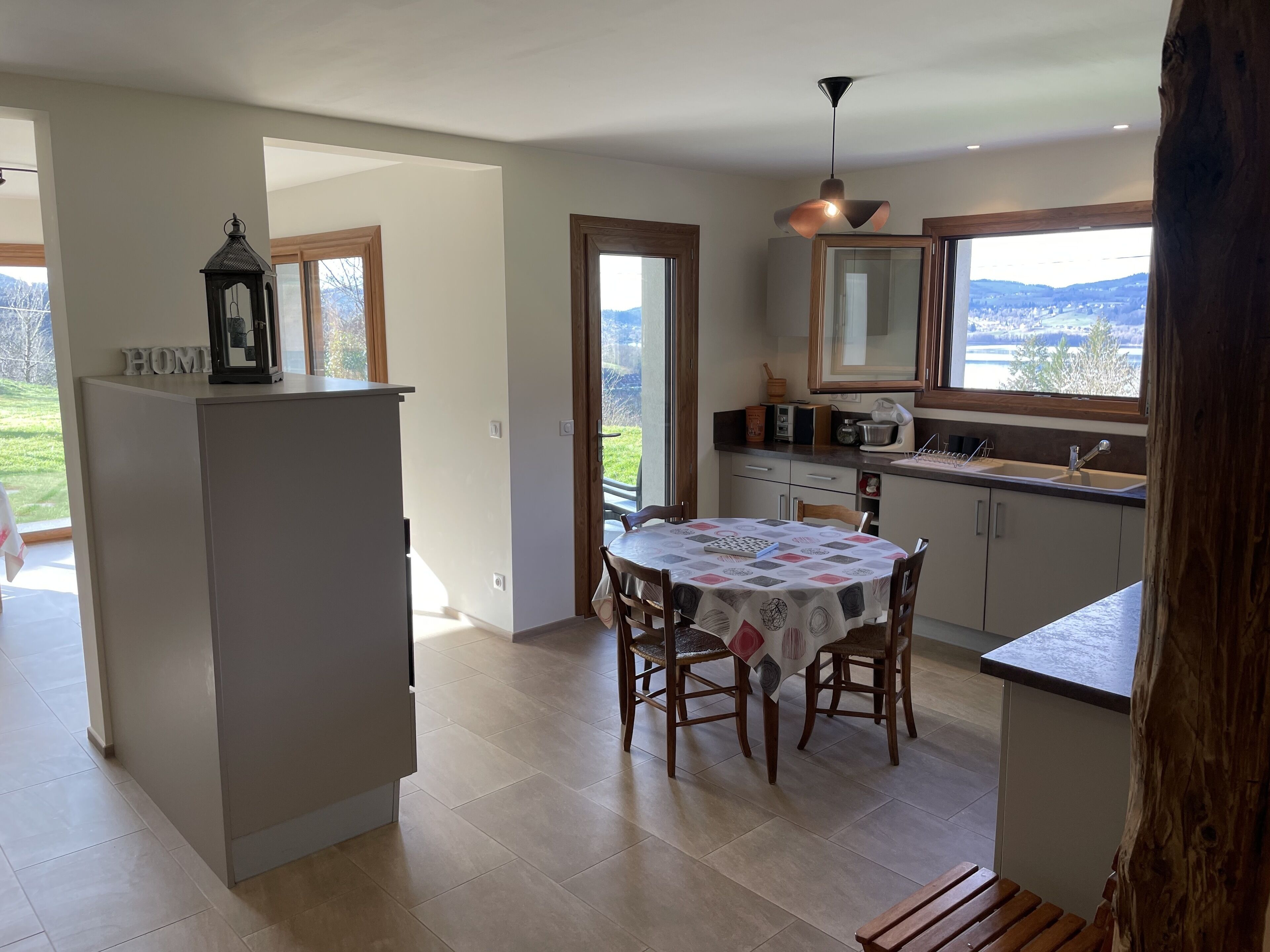 A modern kitchen with a dining area, large windows, and a view of the outdoors.